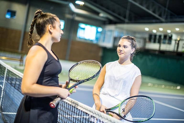 Två unga tennisspelare pratar med varandra framme vid nätet.